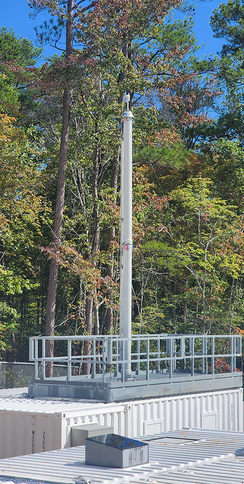 In front of trees, the aerosol stack sticks up from the top of the Aerosol Observing System container at ARM's Bankhead National Forest atmospheric observatory.