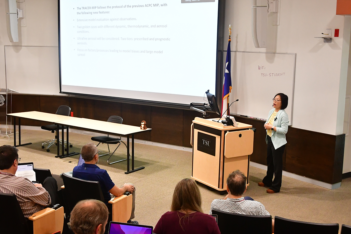 Jiwen Fan presents at the front of an auditorium with a large screen showing a slide on the TRACER-MIP.