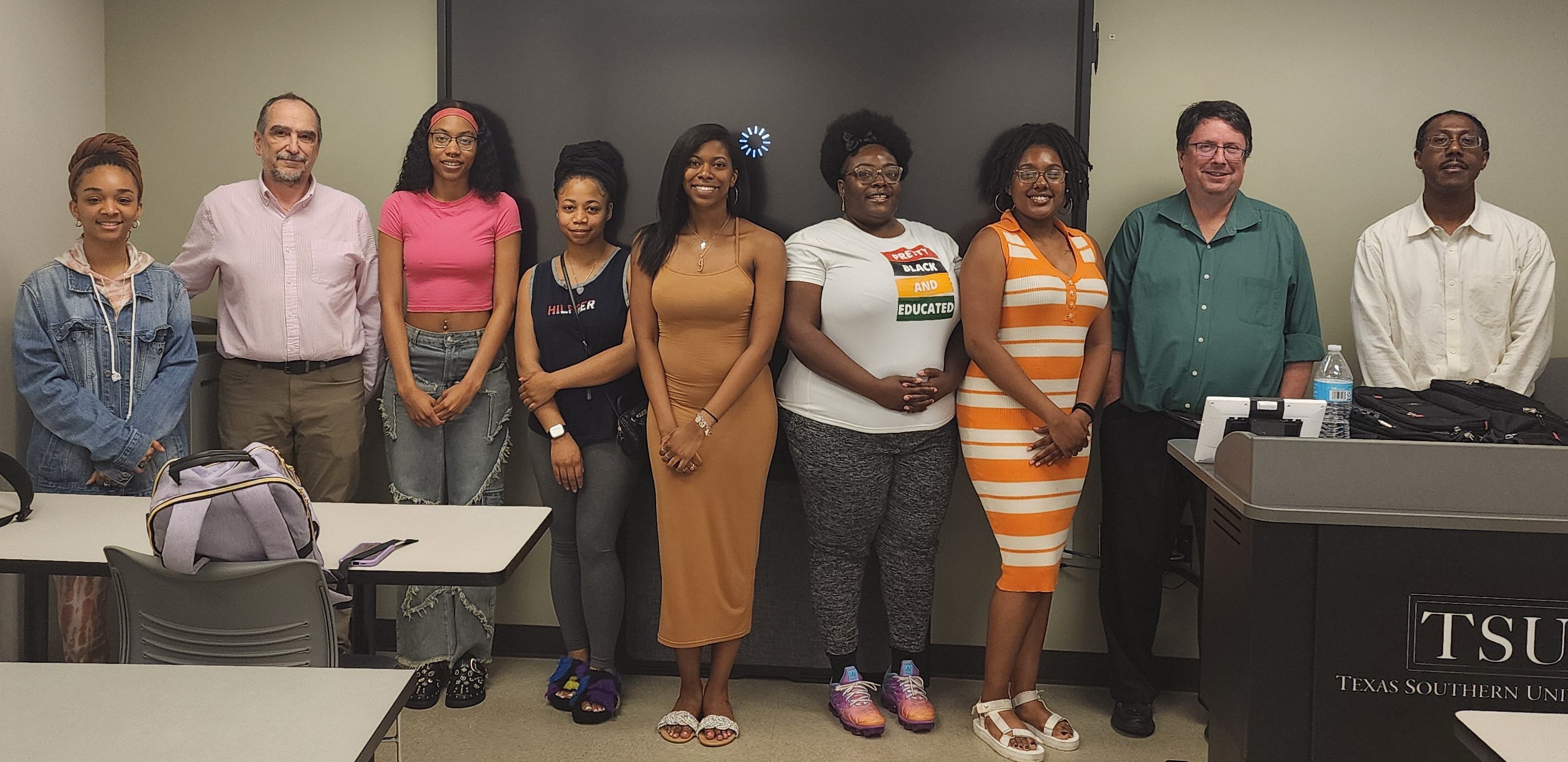 A group of people stand in front of classroom tables and a podium with Texas Southern University across the front.