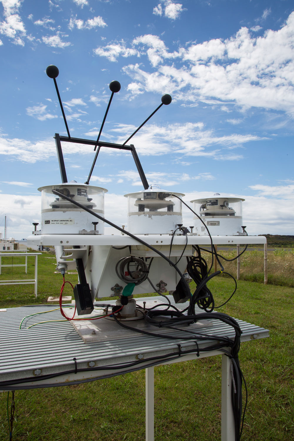 A sky radiation collection of radiometers sits on a table outside at the Eastern North Atlantic observatory as clouds float overhead.