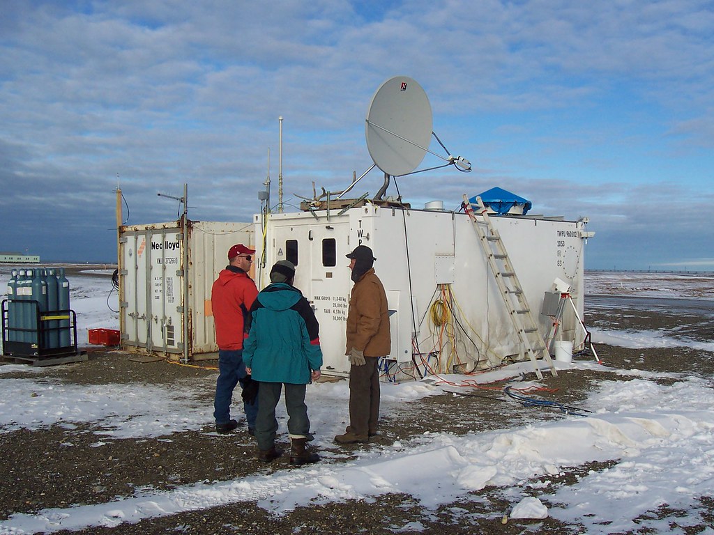 Three people talk outside an instrument container with snow on the ground.