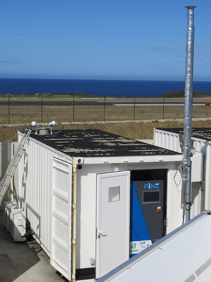 An aerosol stack rises above a container that holds the Portable Ice Nucleation Experiment (PINE) chamber. The Atlantic Ocean is seen beyond the PINE chamber.