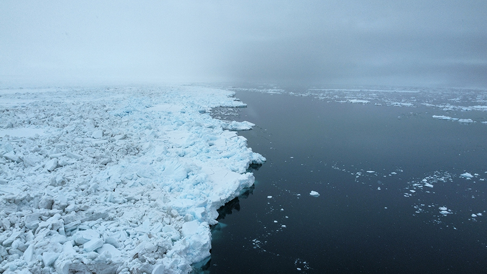 Aerial imagery on a cloudy day shows the edge between landfast sea ice and open water.