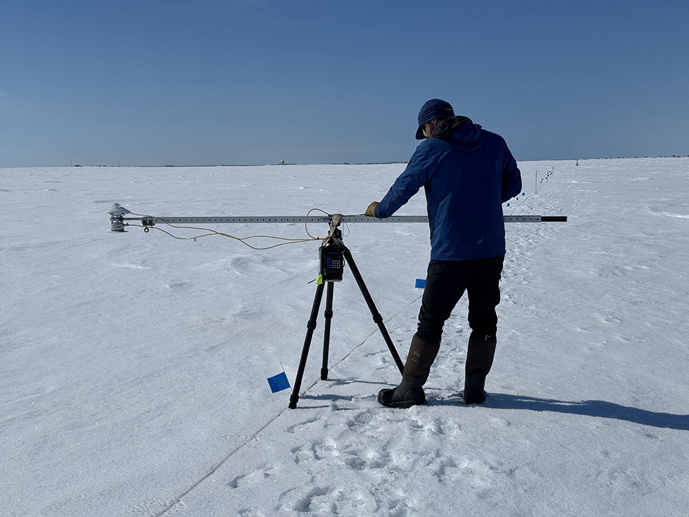 Standing on snow, Philip Wilson makes a broadband albedo measurement on Elson Lagoon during SALVO. The paired pyranometers are on the left end of the boom. Philip is focused on leveling the instrument using a bubble level directly in front of him on the boom.